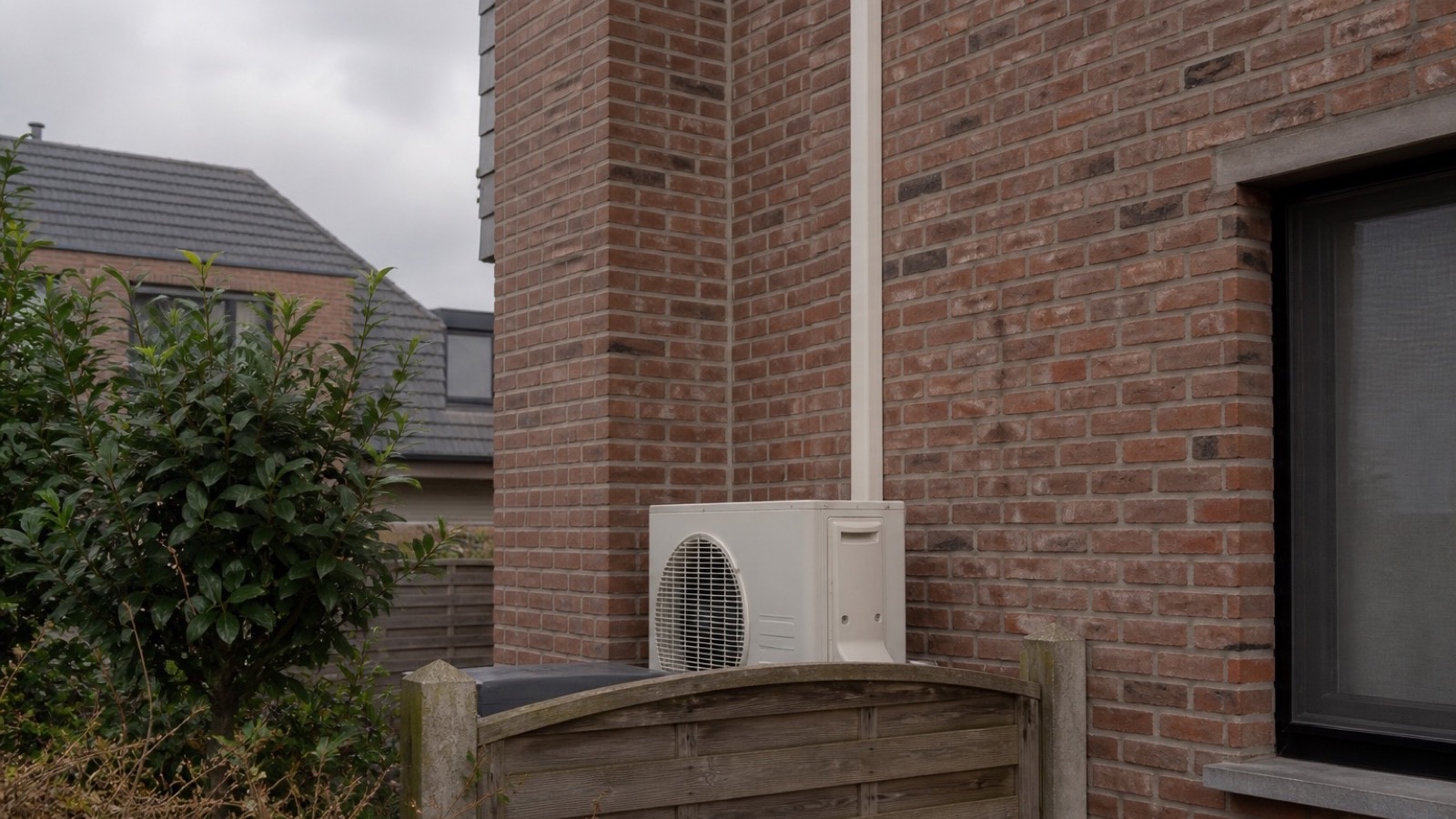 Buitenunit achter een omheining met kabelgoot op de gevel
